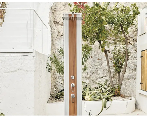 Douche d''extérieur avec habillage en bois devant un mur en pierre avec des plantes