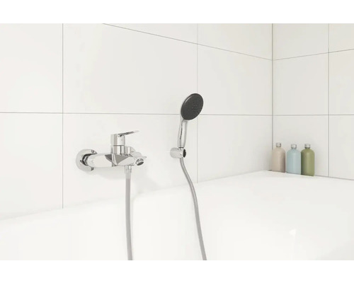 Mitigeur de douche apparent avec douchette à main dans une salle de bains carrelée de blanc.