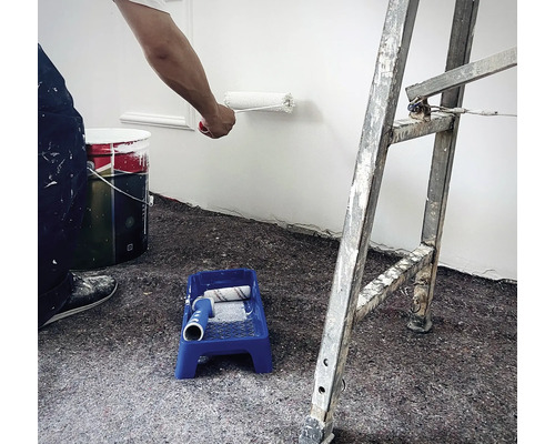 Scène de travaux de peinture : Personne peignant un mur avec un rouleau, un pot de peinture, un bac à peinture avec un rouleau et une échelle dans la pièce.