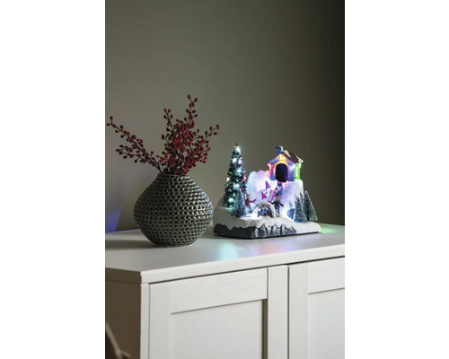 Paysage d''hiver décoratif avec maison, sapin de Noël et patineurs à côté d''un vase avec des baies rouges sur une armoire