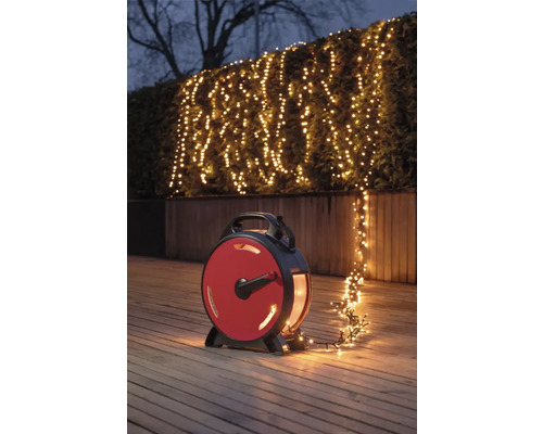 Scène avec une guirlande lumineuse sur un enrouleur éclairant un arbuste dans le jardin.
