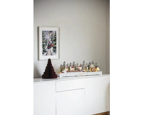 Dekoratives Weihnachtsdorf mit Zug auf einer weißen Kommode mit einem Bild von einem Zug an der Wand.