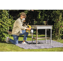 Un homme utilise un pistolet à peinture à l''extérieur pour laquer une table.