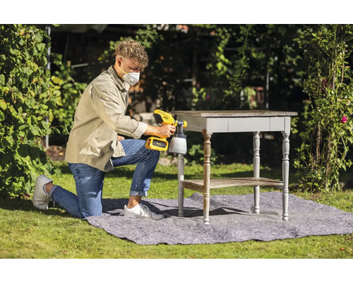 Un homme utilise un pistolet à peinture à l''extérieur pour laquer une table.