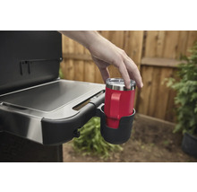 Eine Person stellt einen roten Becher mit Griff in einen Getränkehalter an einem Grill.