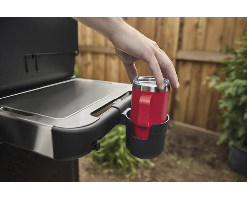 Eine Person stellt einen roten Becher mit Griff in einen Getränkehalter an einem Grill.