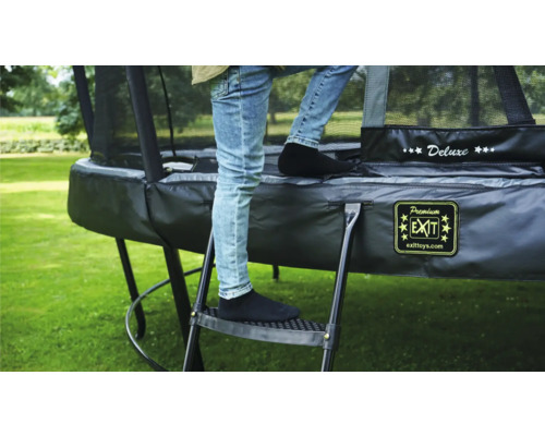 Une personne monte sur un trampoline de jardin à l''aide d''une échelle.