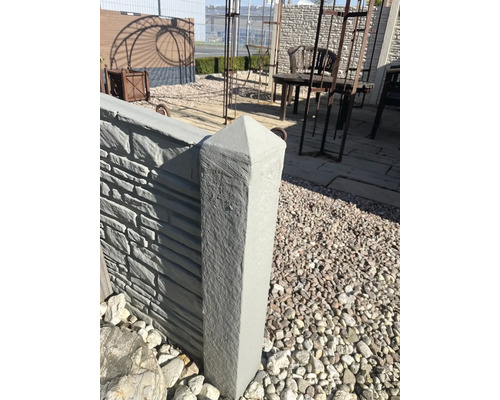 Poteau de clôture en béton avec sommet pyramidal dans un espace jardin.