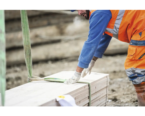 Bauarbeiter hebt Holzstapel mit Hebegurt.