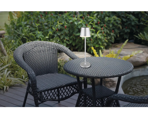 Gartenszene mit Rattansessel, Tisch und silberfarbener Tischleuchte.