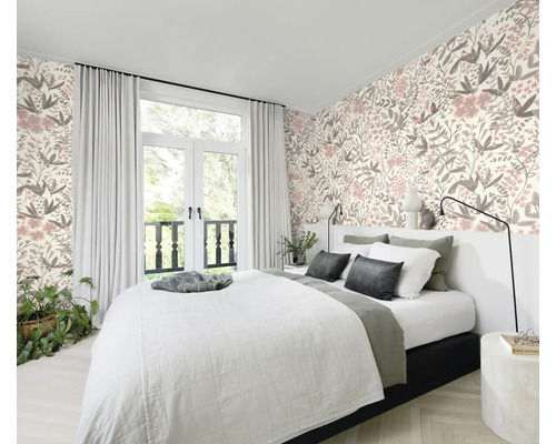 Chambre à coucher avec lit devant un papier peint à motifs floraux et une fenêtre avec des rideaux.