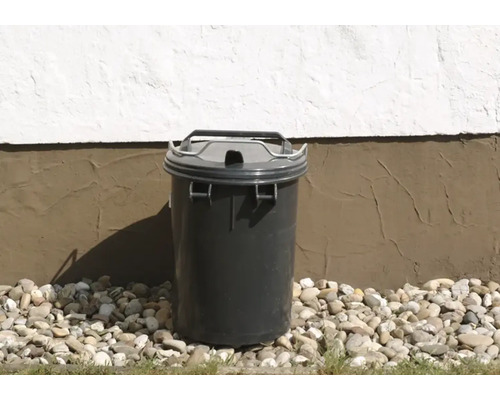 Poubelle grise avec couvercle devant un mur de maison sur du gravier