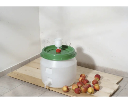 Gärbehälter mit Gärspund und Äpfeln auf Holzbrett