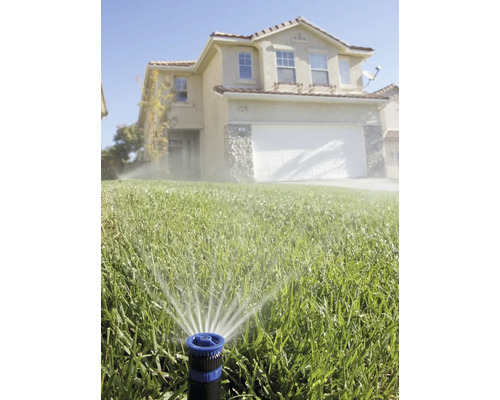 Arroseur de pelouse arrosant une pelouse devant une maison
