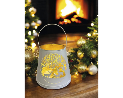 Lanterne décorative avec motif de cerf et poignée devant une cheminée et un sapin de Noël.