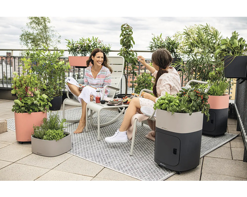 Szene auf einer Dachterrasse mit zwei Frauen, Sitzmöbeln und verschiedenen Pflanzgefäßen mit Pflanzen