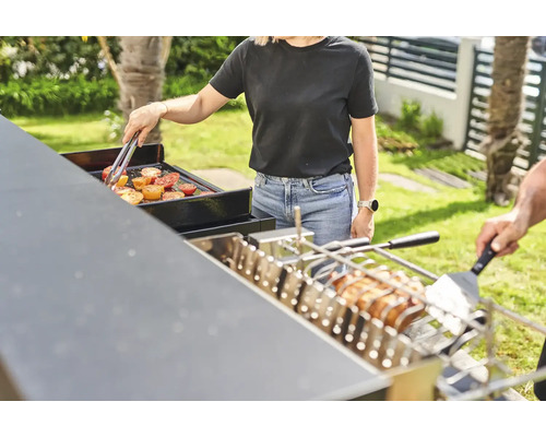 Personen grillen Gemüse und Fleisch auf einem Grill im Freien.
