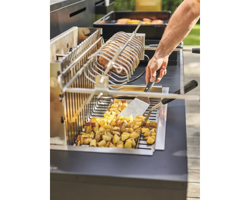 Person bereitet Kartoffeln und Fleisch auf einem Grill mit Drehspieß zu.