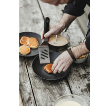 Une personne retourne des crêpes avec une spatule sur une assiette.