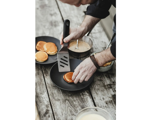 Une personne retourne des crêpes avec une spatule sur une assiette.