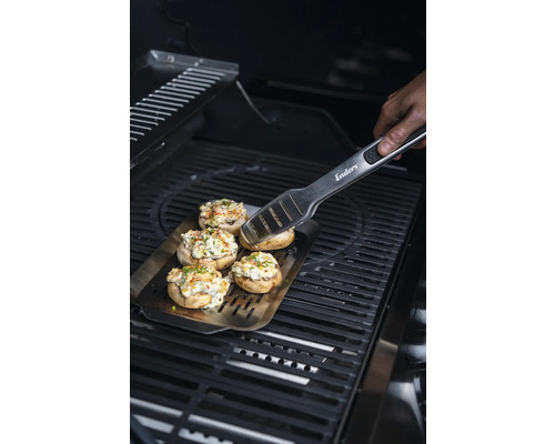 Champignons farcis sur une plaque de cuisson avec une pince à barbecue sur un gril