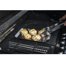 Champignons farcis sur une plaque de gril avec une pince de barbecue sur un gril