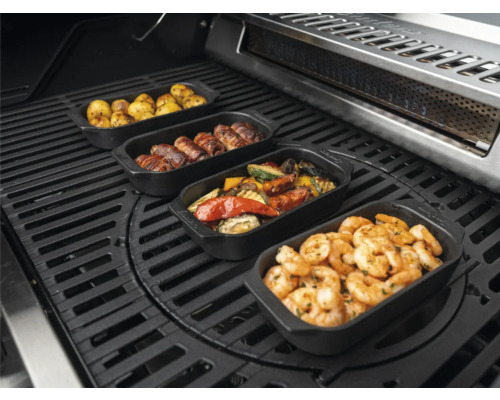 Divers plats dans des plats à griller sur un barbecue, y compris des pommes de terre, des rouleaux de viande, des légumes et des crevettes.