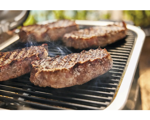 Quatre steaks sur une grille de barbecue avec dégagement de fumée.