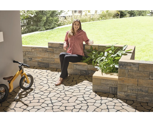 Espace de jardin avec dalles de sol imitation pierre naturelle, mur et une femme assise sur un banc