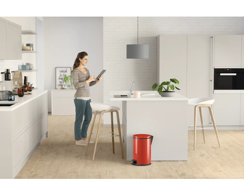 Cuisine claire avec îlot central, poubelle à pédale rouge et une femme utilisant une tablette.