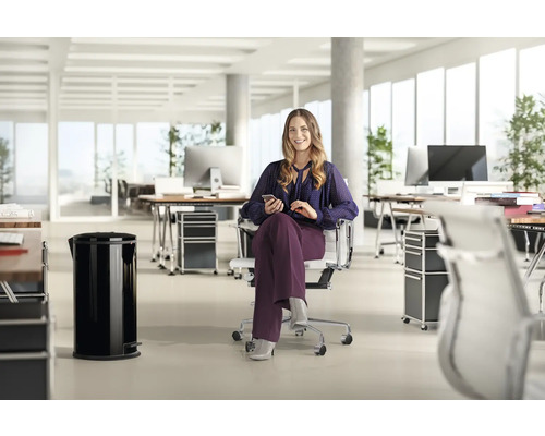 Bureau lumineux avec bureaux, caissons à roulettes, poubelle à pédale et une femme sur un fauteuil de bureau