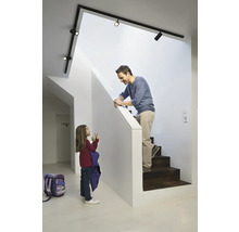 Ein Vater auf einer Treppe spricht mit seiner Tochter im Flur unter einer Schienenleuchte.