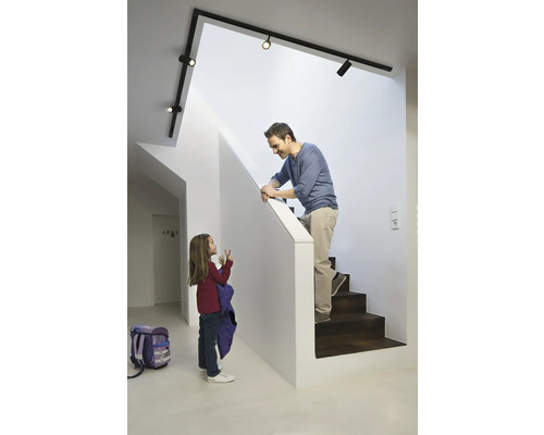 Ein Vater auf einer Treppe spricht mit seiner Tochter im Flur unter einer Schienenleuchte.