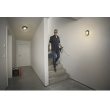 Flur mit Deckenleuchte, Wandleuchte und Mann, der die Treppe hinuntergeht