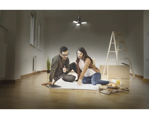 Un couple est assis par terre dans une pièce lumineuse et planifie la rénovation avec un plan et un plafonnier.