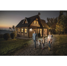 Familie geht an einem mit einem Aussenstrahler beleuchteten Holzhaus vorbei.