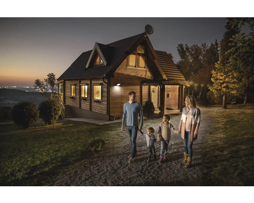 Familie geht an einem mit einem Aussenstrahler beleuchteten Holzhaus vorbei.