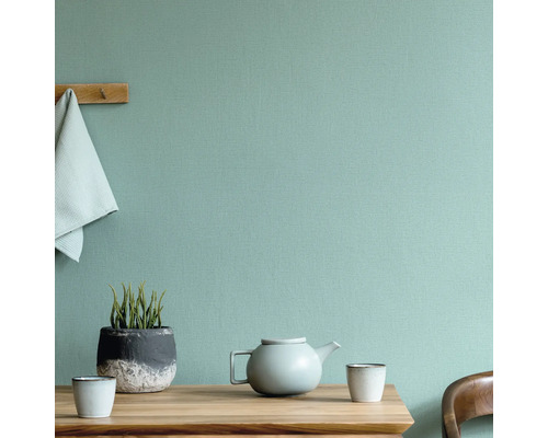 Scène avec table, théière, tasses, plante et serviette devant un mur structuré