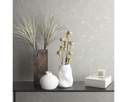 Dekoratives Stillleben mit Vasen, Zierpflanzen, Kerze und Buch auf einem Tisch.