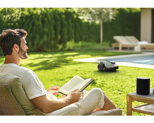 Mann liest Buch im Garten mit Mähroboter
