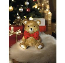 Figurine décorative ours en peluche avec nœud papillon devant un sapin de Noël