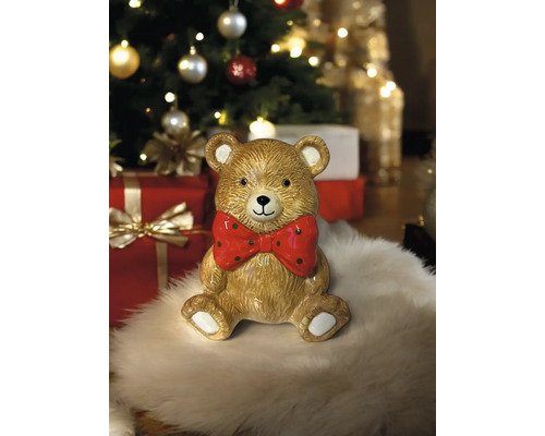 Figurine décorative ours en peluche avec nœud papillon devant un sapin de Noël