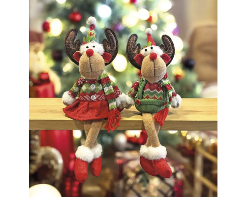 Deux figurines décoratives de rennes aux motifs de Noël sont assises sur une étagère devant un sapin de Noël.