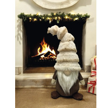 Dekorative Figur eines Weihnachtswichtels vor einem Kamin mit brennendem Holz und Weihnachtsgeschenken.