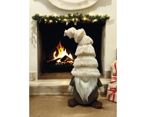 Dekorative Figur eines Weihnachtswichtels vor einem Kamin mit brennendem Holz und Weihnachtsgeschenken.