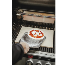 Une pizza est placée sur une pierre à pizza dans le gril à l''aide d''une pelle à pizza.