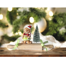 Scène décorative avec figurine bonhomme en pain d’épices, petit sapin et rouleau à pâtisserie devant un sapin de Noël