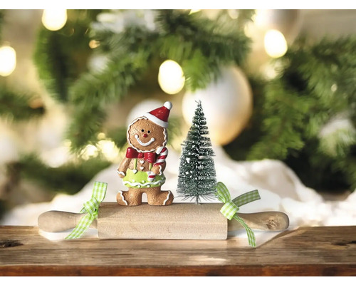 Dekorative Szene mit Lebkuchenmannfigur, kleinem Tannenbaum und Nudelholz vor einem Weihnachtsbaum