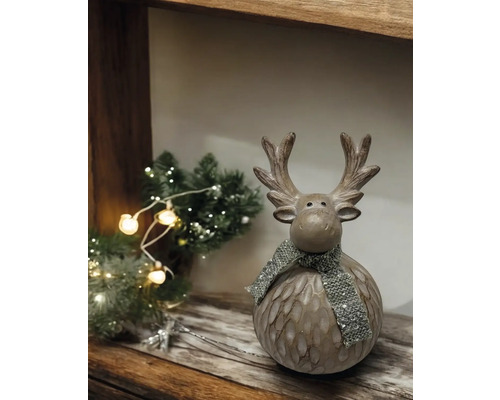 Dekorativer Elch mit Schal auf einem Holzregal mit Weihnachtsbaum und Lichtern