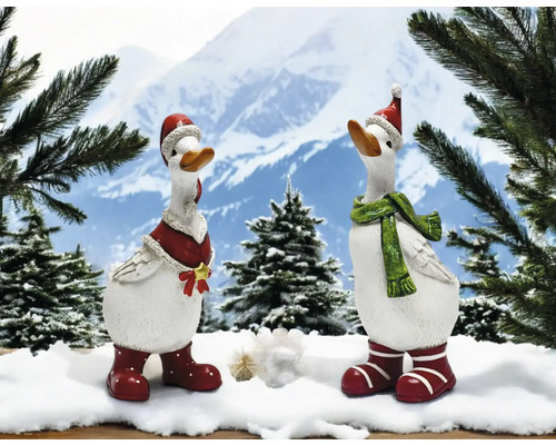 Zwei dekorative Gänsefiguren mit Weihnachtsmützen und Winteraccessoires vor Bergkulisse.